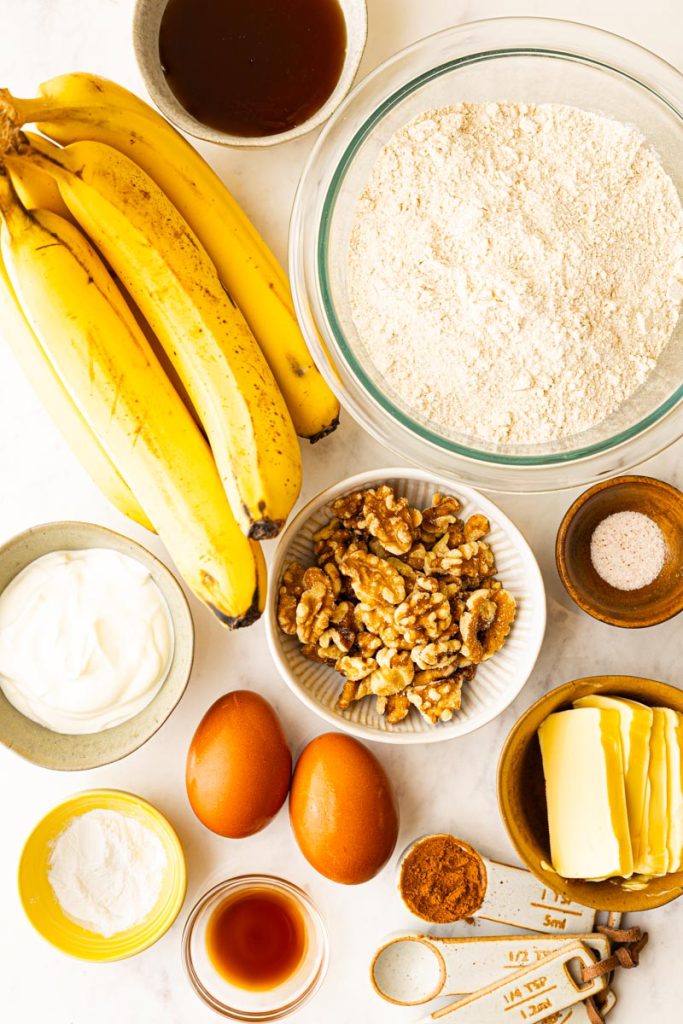 Ingredients to make healthy banana bread: ripe bananas, flour, eggs, butter, honey, greek yogurt, vanilla extract, cinnamon, baking soda, and salt.