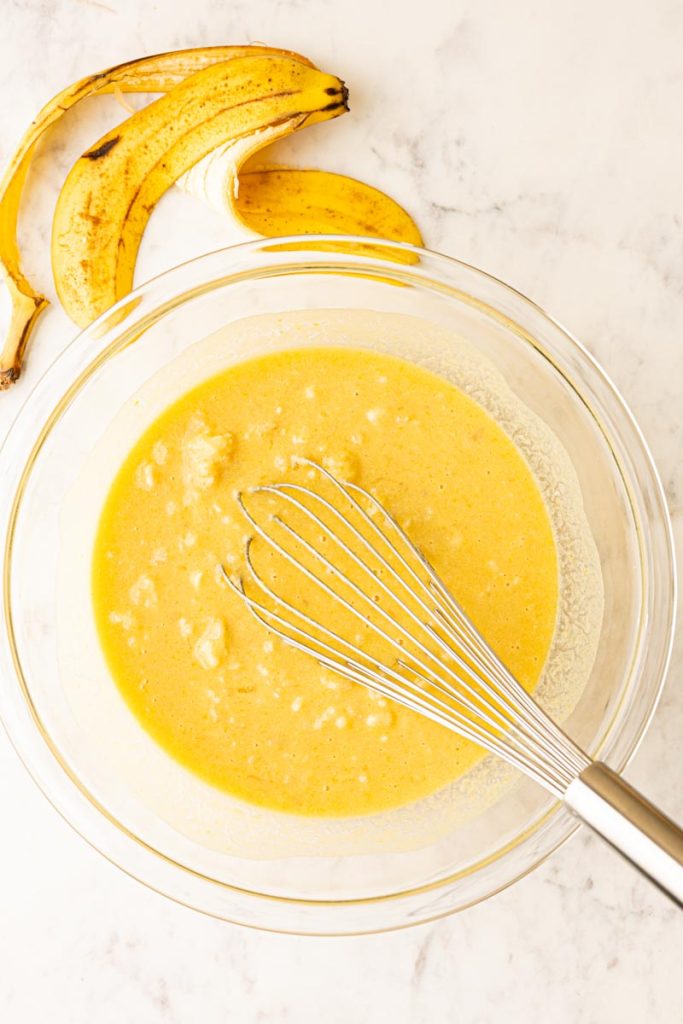 Wet ingredients for banana bread whisked together in a glass mixing bowl with a whisk.