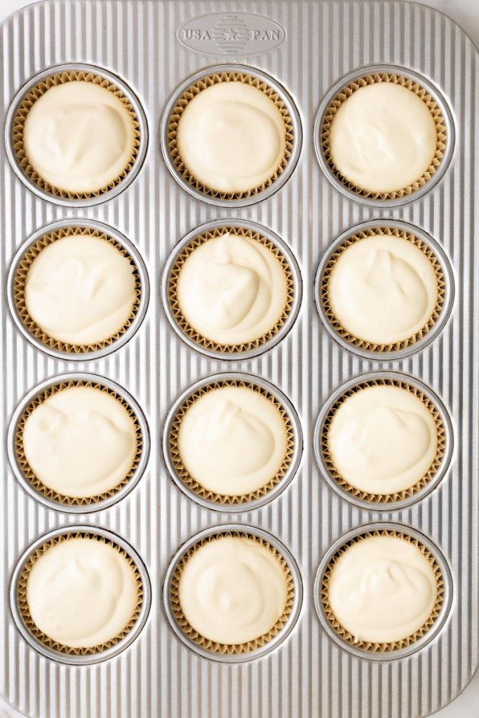 Muffin pan filled with 12 mini cheesecakes before baking.