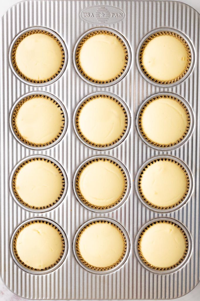 Muffin pan filled with 12 mini cheesecakes after baking.