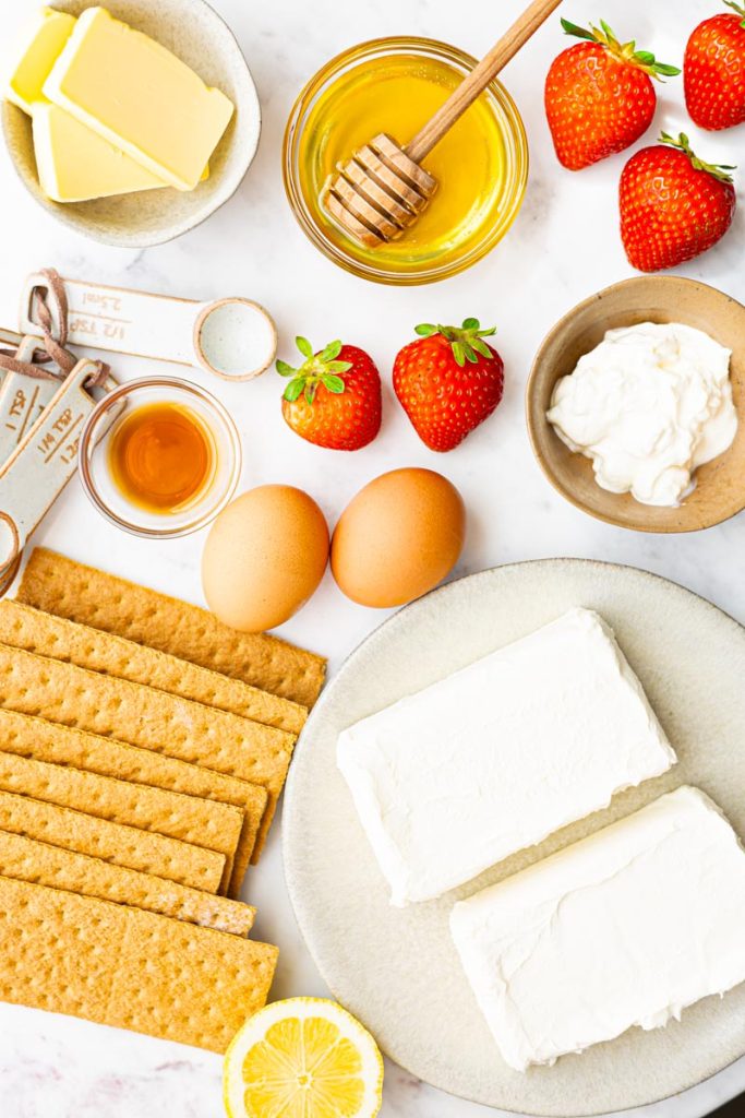 Ingredients to make mini cheesecakes: cream cheese, sour cream, butter, honey, eggs, vanilla extract, and graham crackers.
