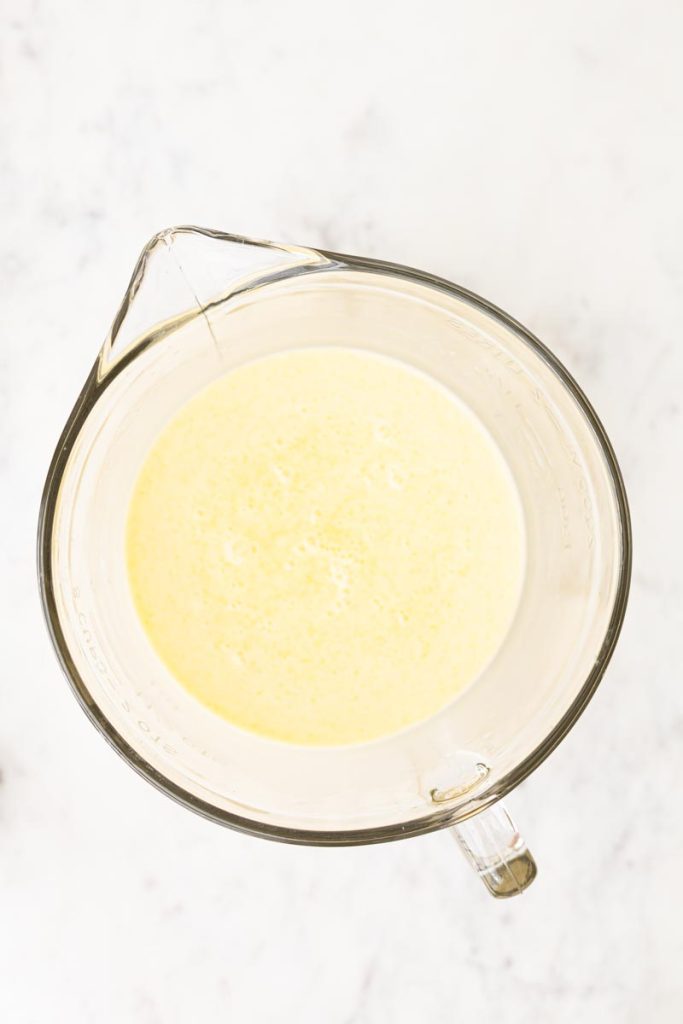 A large measuring cup with wet ingredients to make fluffy whole wheat waffles.